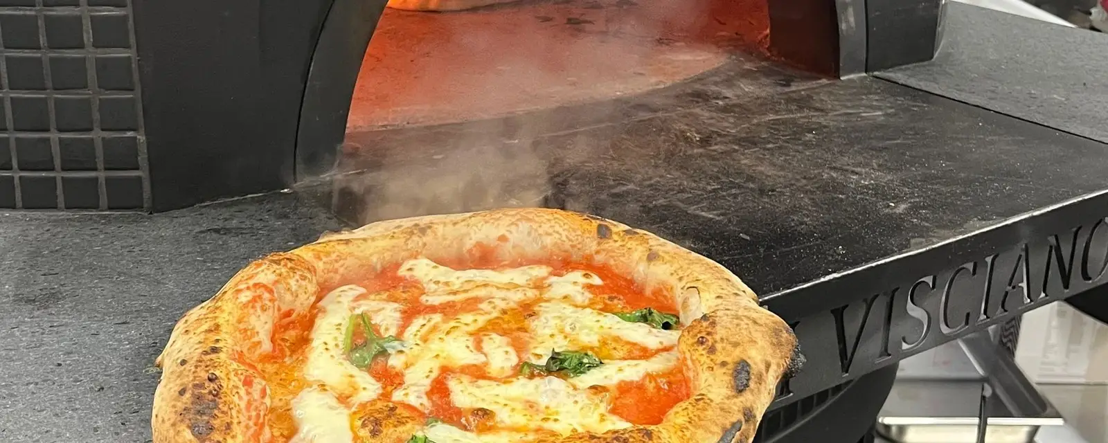 A pizza on the peel in front of the wood-fire oven