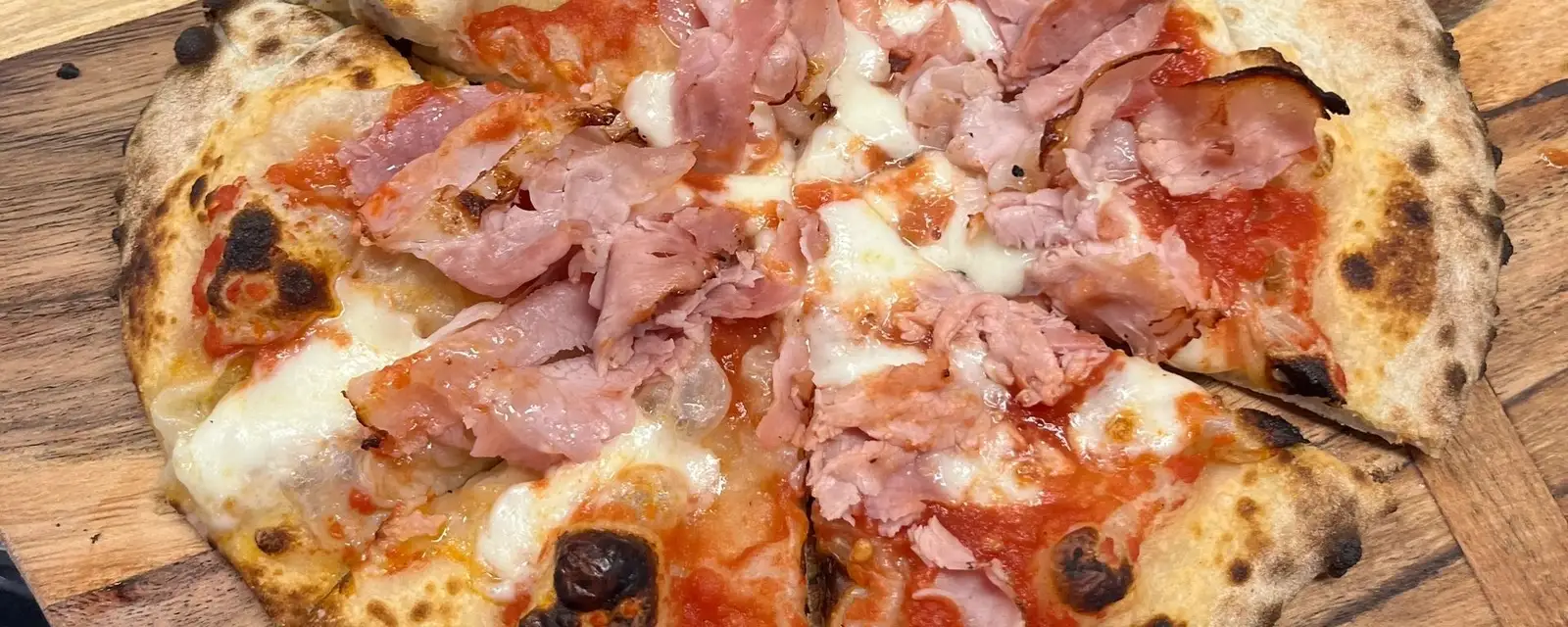 A wood-fired pizza with ham and mozzarella on a wooden board